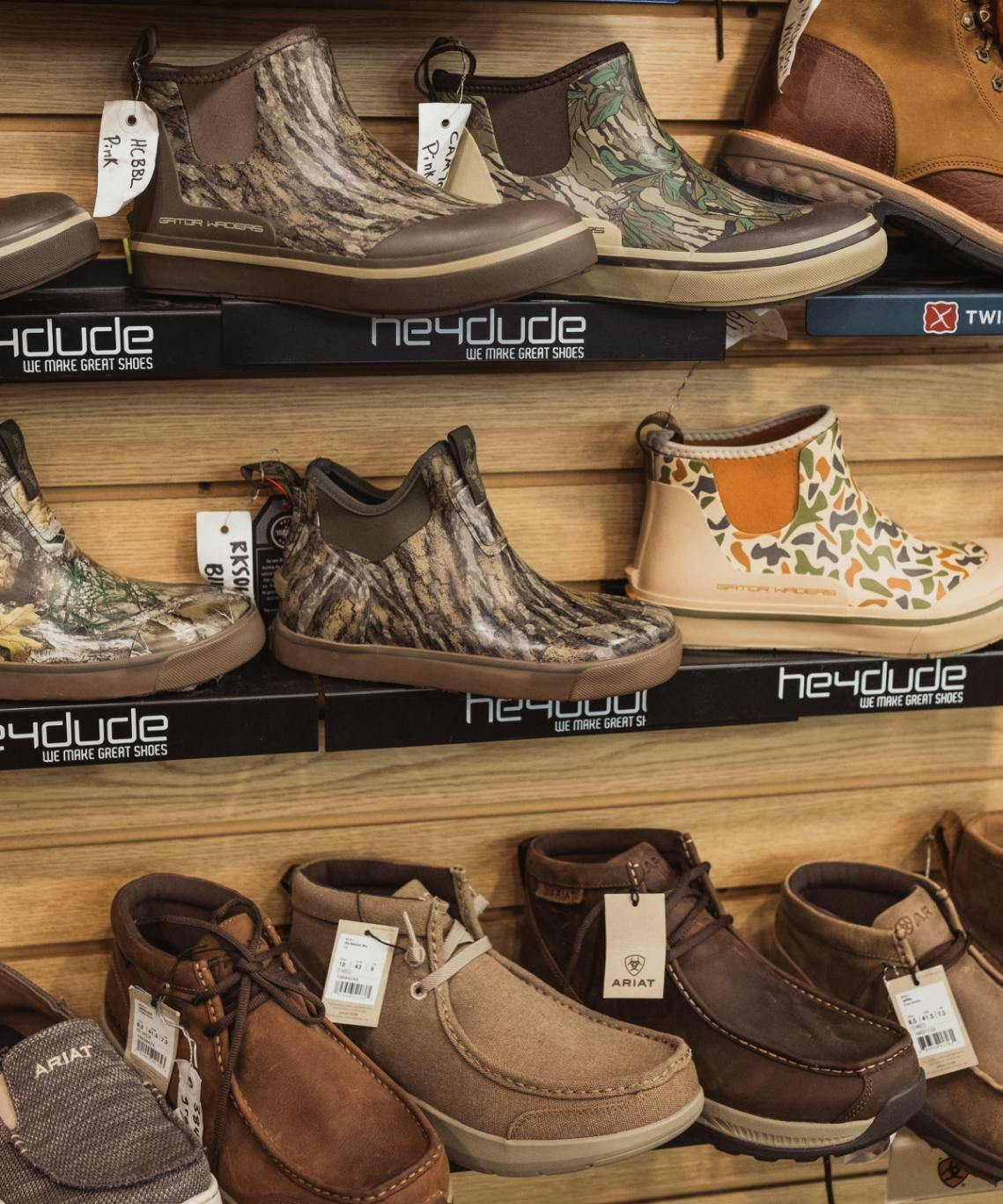 multiple pairs of camoflauge patterned, heydude brand, boat shoes. there are also leather ariat shoes on the shelf below | anderson's general store