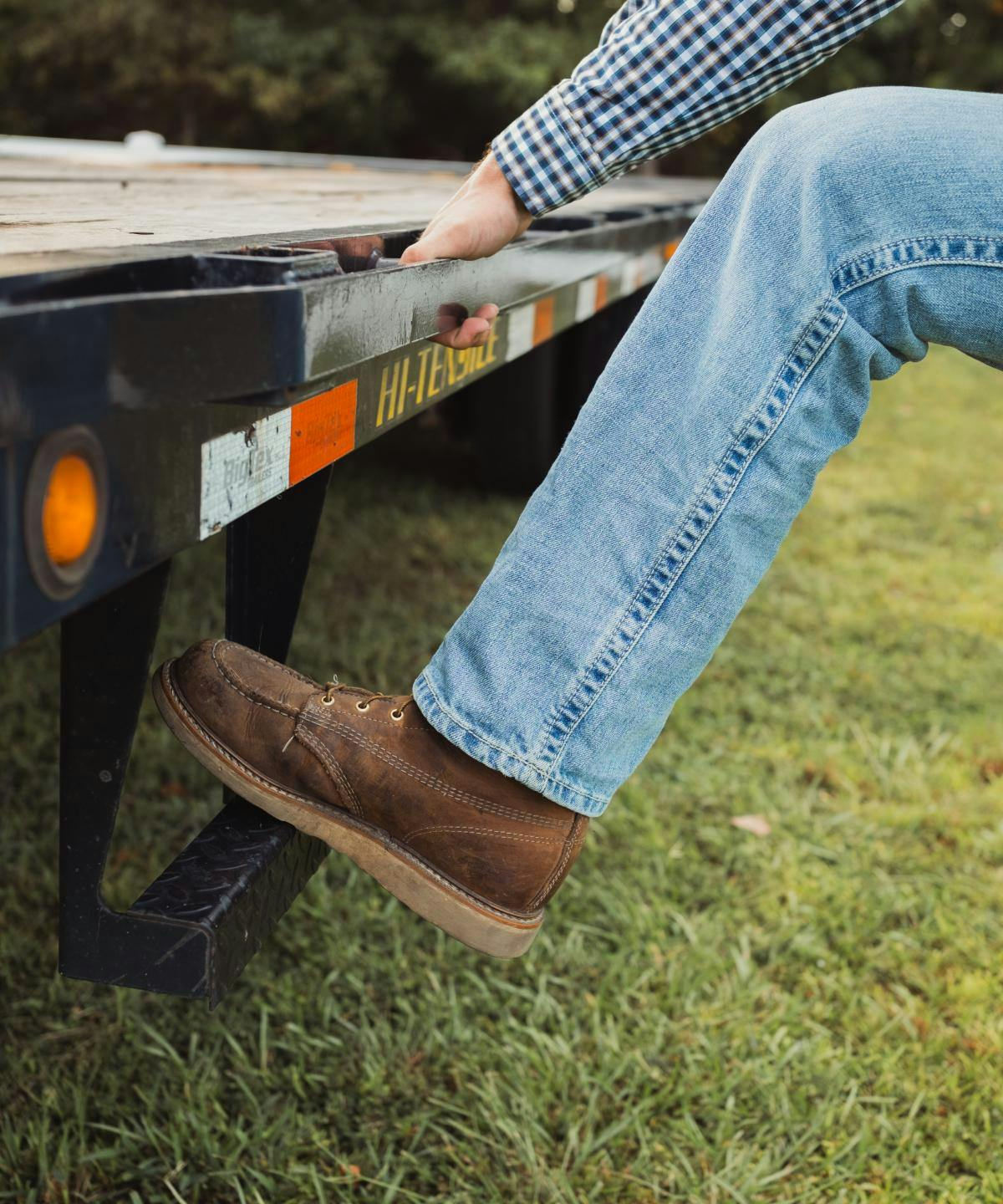 man in boots and jeans stepping up onto the back of a flatbead trailer | anderson's general store
